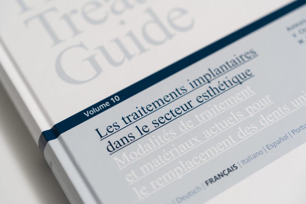 Close-up of a dental treatment guide book titled "Les traitements implantaires dans le secteur esthétique," highlighting dental implant procedures and materials.