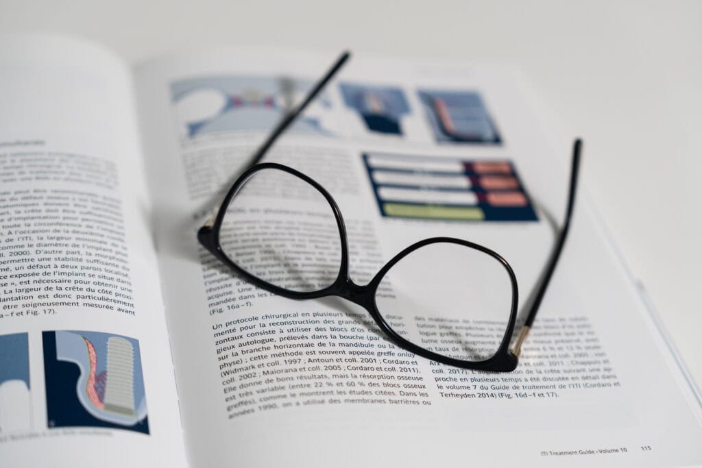 Lunettes posées sur un ouvrage d’implantologie avec illustrations cliniques