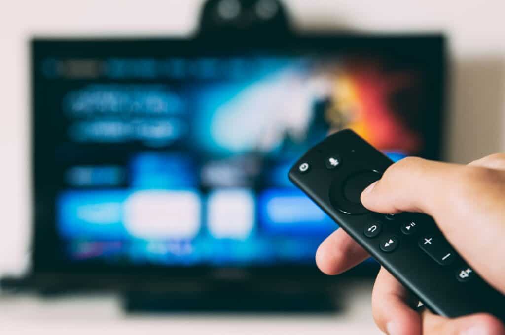 Close-up of a hand holding a remote control pointing at a blurred TV screen displaying digital content, emphasizing home entertainment and media management.