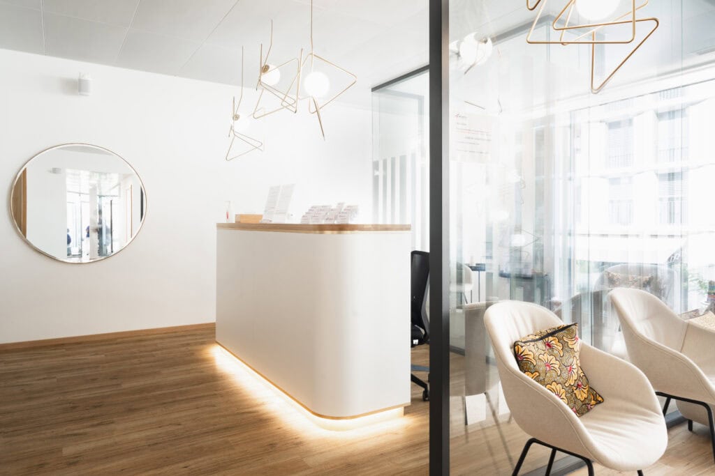 Bright and welcoming dental clinic reception featuring contemporary design, elegant lighting fixtures, and cozy chairs with decorative pillows for patient comfort.