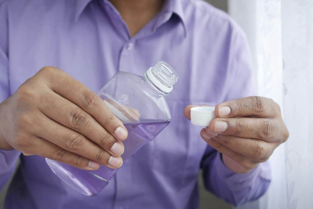 Close-up of a person holding a small bottle of mouthwash and a cap, demonstrating dental hygiene practices at Ardentis dental clinic.