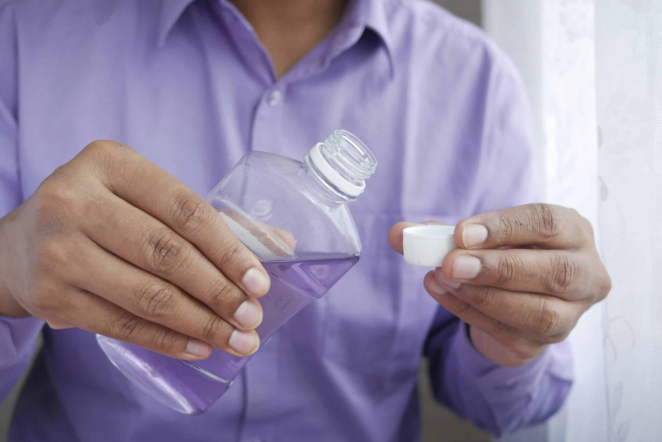 Close-up of a person holding a small bottle of mouthwash and a cap, demonstrating dental hygiene practices at Ardentis dental clinic.
