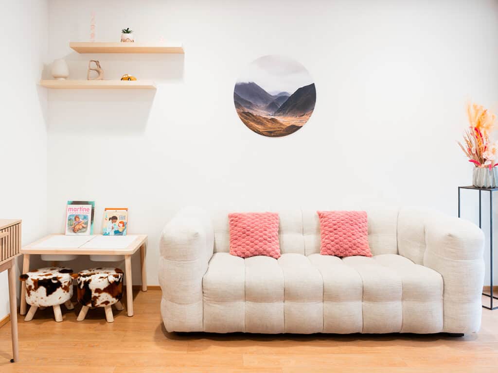 Sofa moderne dans un salon minimaliste avec décoration élégante, mur blanc, étagères, tableau rond et coussins roses, ambiance chaleureuse et épurée.
