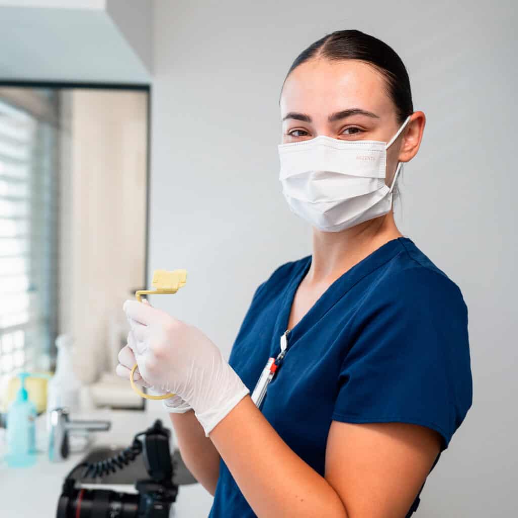 Praticienne en soins dentaires portant un masque et des gants dans un cabinet médical moderne, prête à effectuer un traitement dentaire.