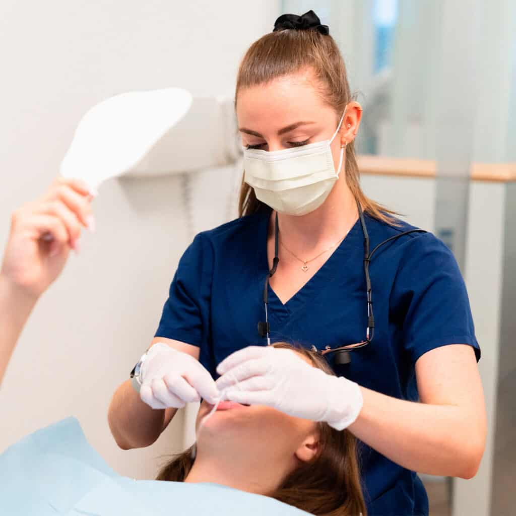 Praticienne en soins dentaires portant un masque et des gants, effectuant un traitement dentaire précis sur une patiente allongée.