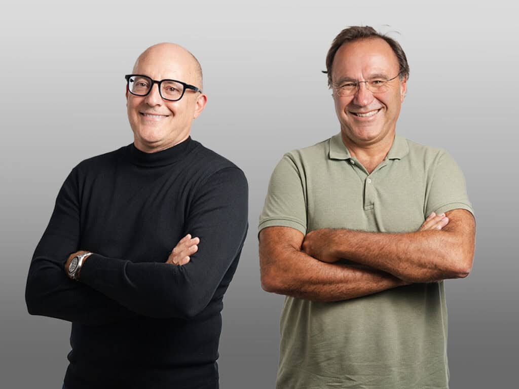 Homme d'affaires en technologie dentaire portant des lunettes noires et un pull noir, à côté d'un autre homme en polo vert clair, tous deux souriants.
