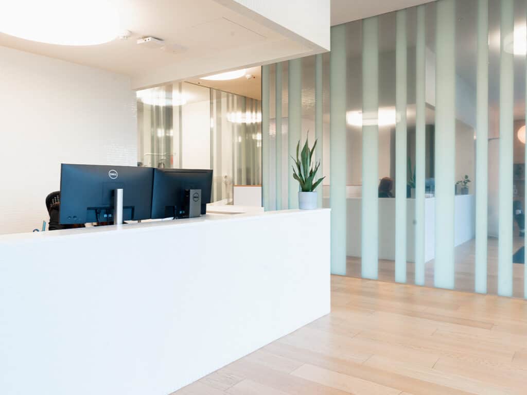 Accueil professionnel avec comptoir blanc, ordinateurs et décoration végétale dans un espace moderne et lumineux.
