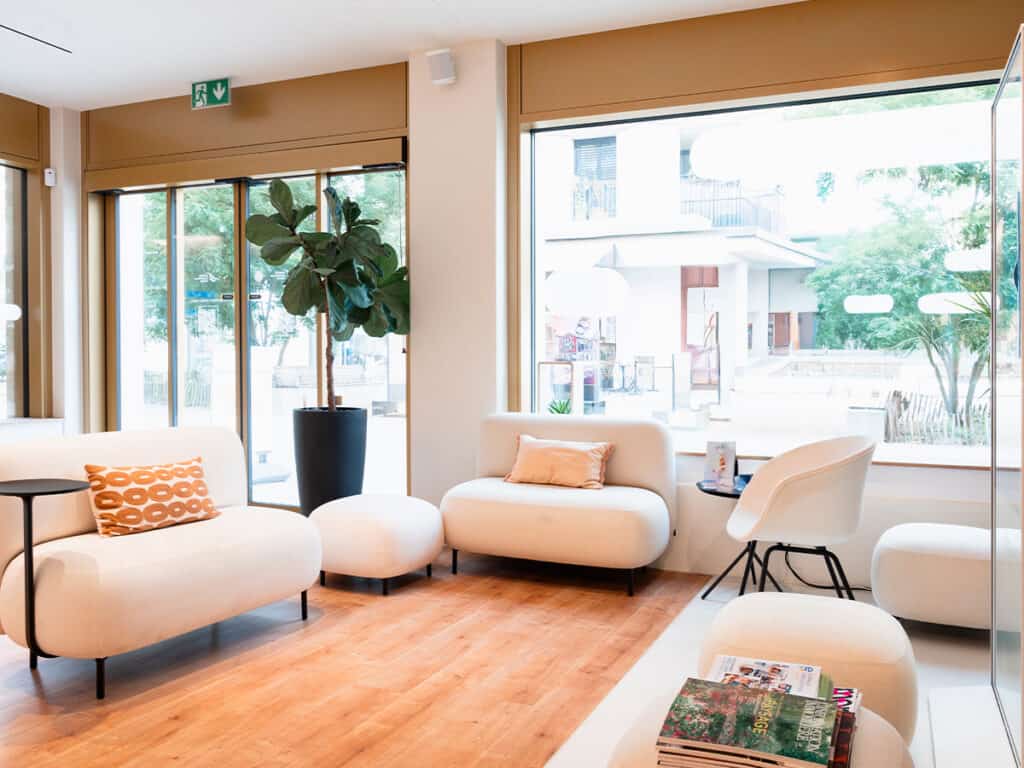 Ardentis, centre dentaire à Genève, avec salle d'attente lumineuse et confortable, mobilier contemporain, grande fenêtre offrant une vue agréable, ambiance accueillante pour patients.