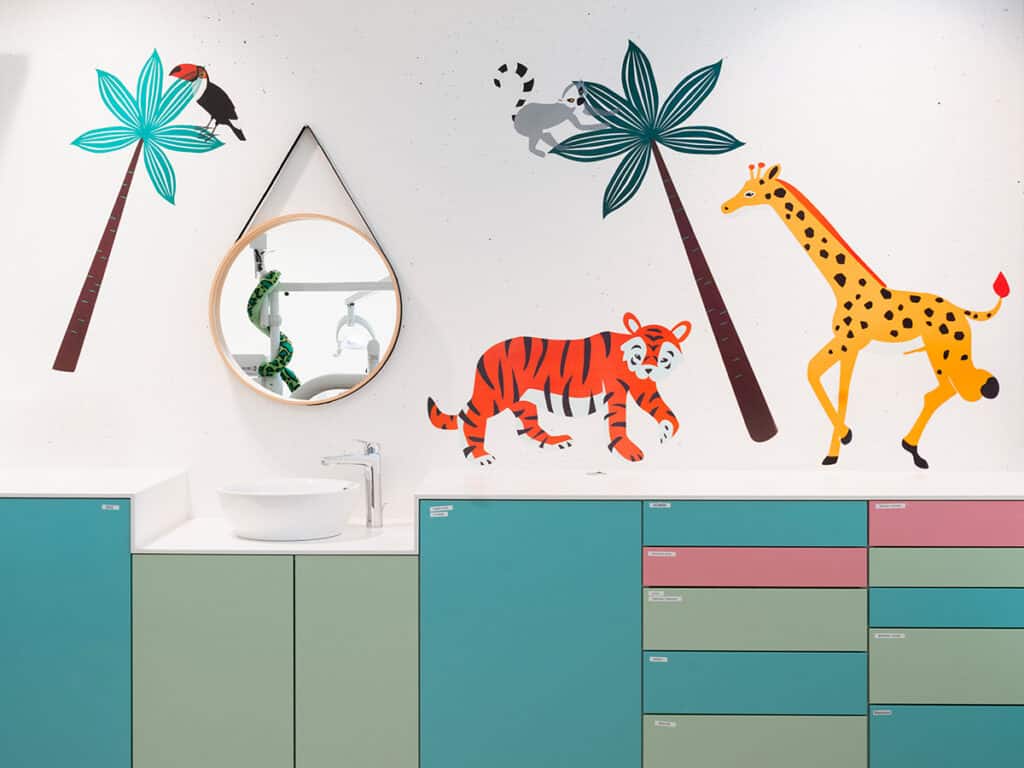 Salle de bain pour enfants décorée avec des illustrations d'animaux sauvages, palmiers colorés et meubles modernes, créant un espace ludique et accueillant.