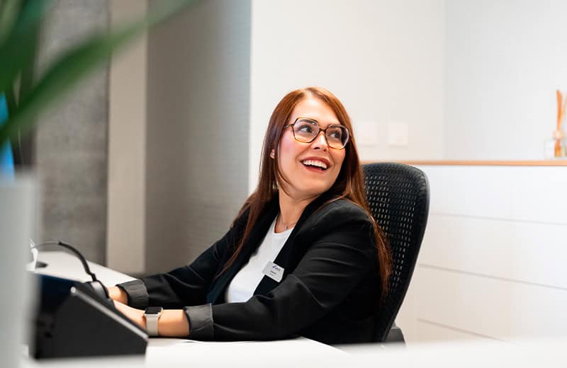 Friendly female receptionist at Ardentis dental clinic smiling while assisting patients at the reception desk.