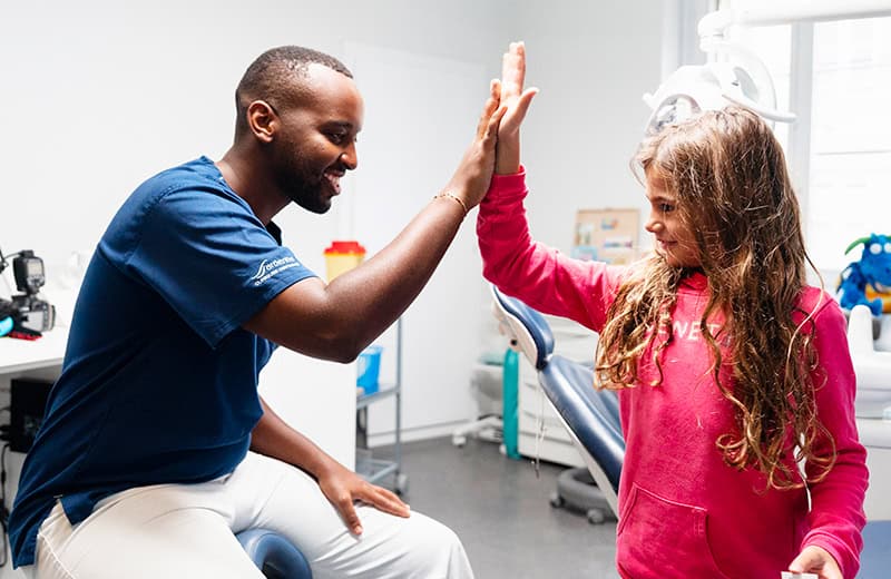 Dentist and young girl giving a high-five in a dental clinic, promoting friendly dental care and patient comfort.