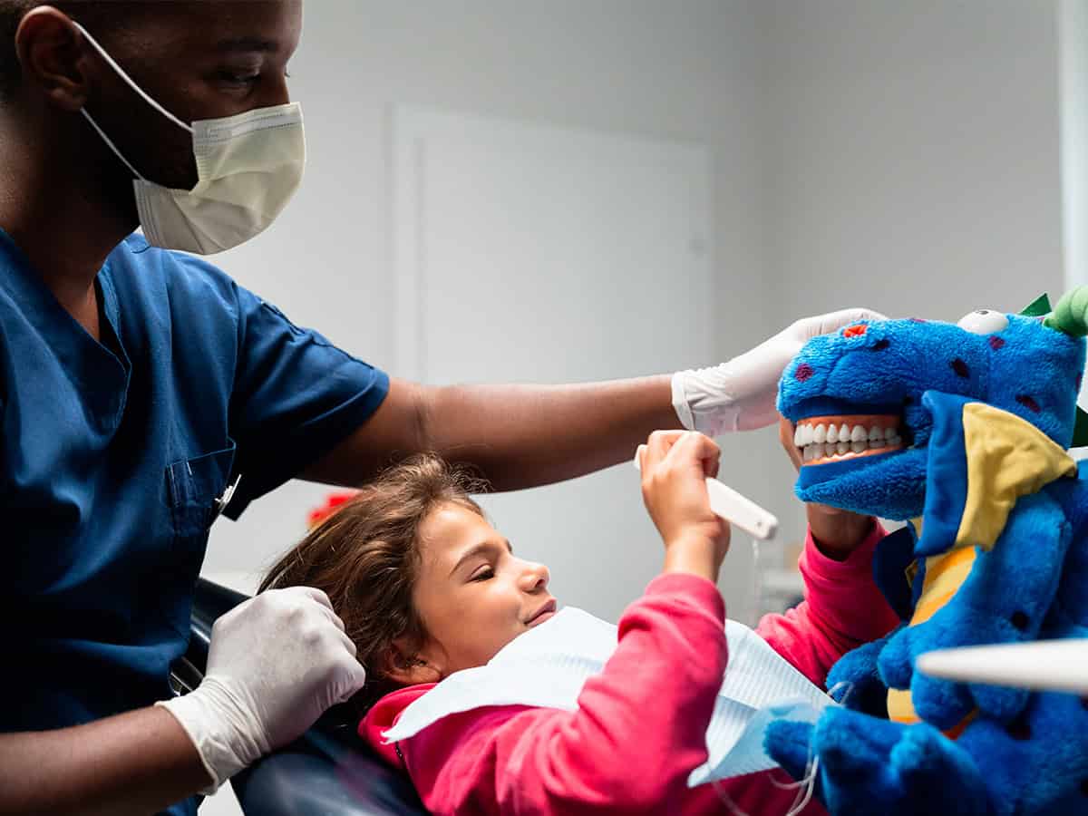 Dentiste rassurant une enfant en consultation avec une peluche éducative