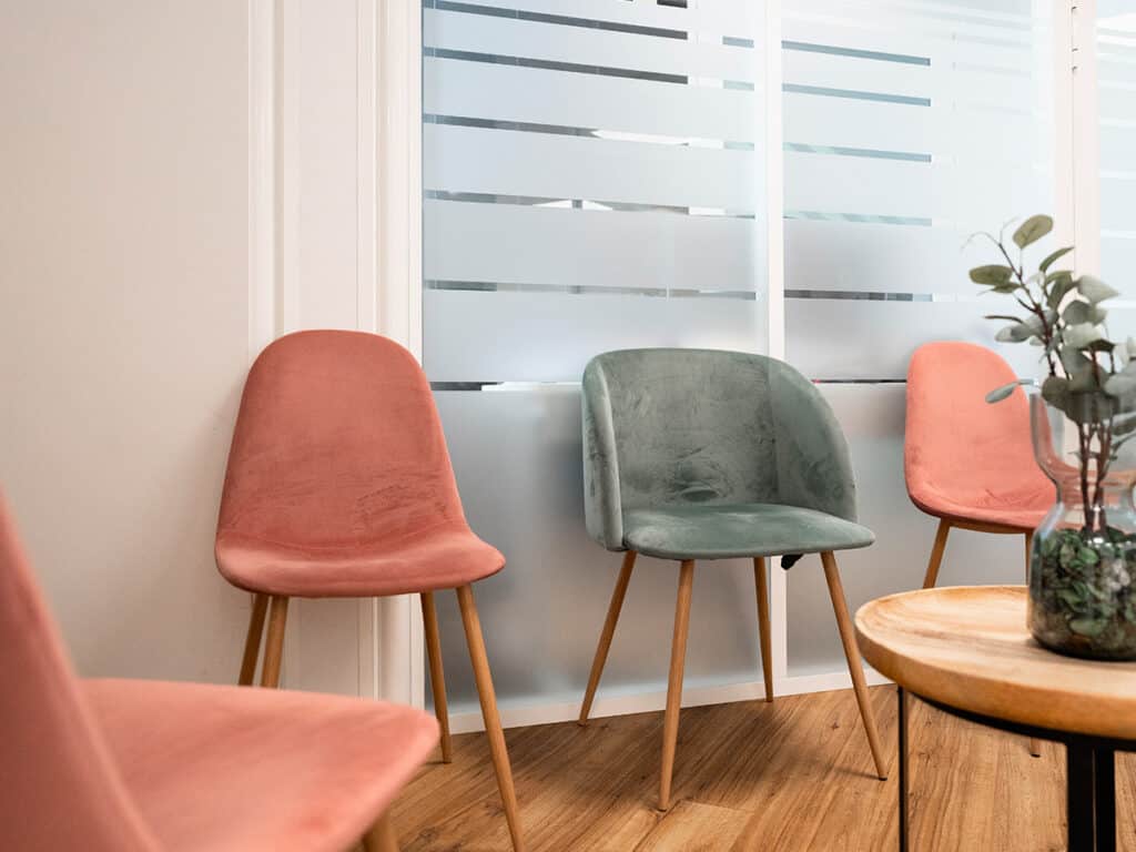 Comfortable waiting area in a dental clinic featuring colorful chairs, wooden flooring, and natural light from large windows.