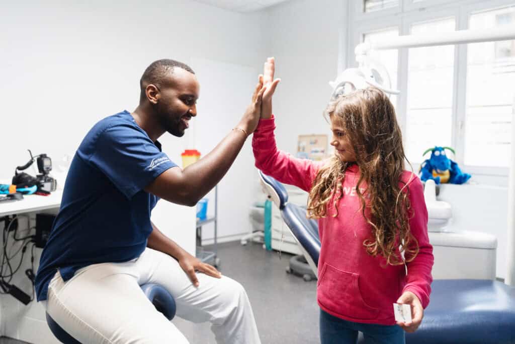 Pediatric dental consultation at Ardentis clinic with a dentist and young girl giving a high five in a bright, modern dental office.