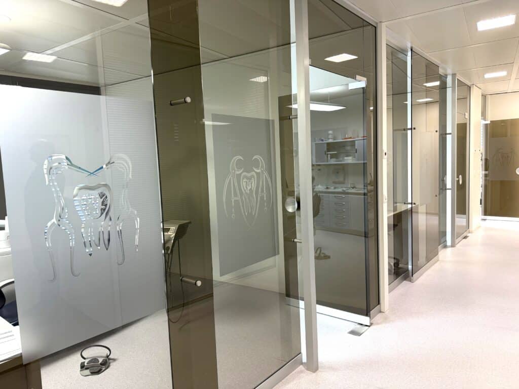Porte en verre avec logo dentaire gravé, intérieur d'une clinique dentaire moderne avec équipements professionnels.