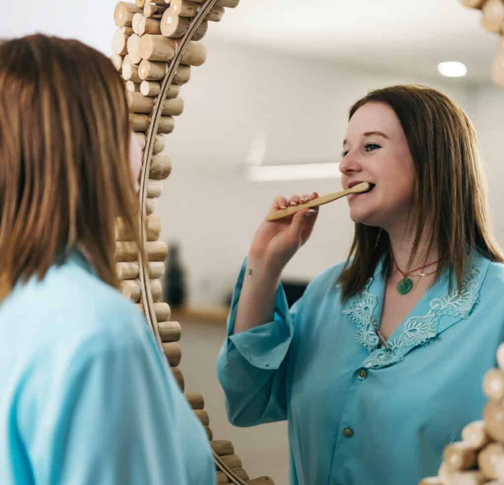 Femme souriante en blouse dentaire se regardant dans un miroir dentaire, illustrant les soins dentaires professionnels chez Ardentis.