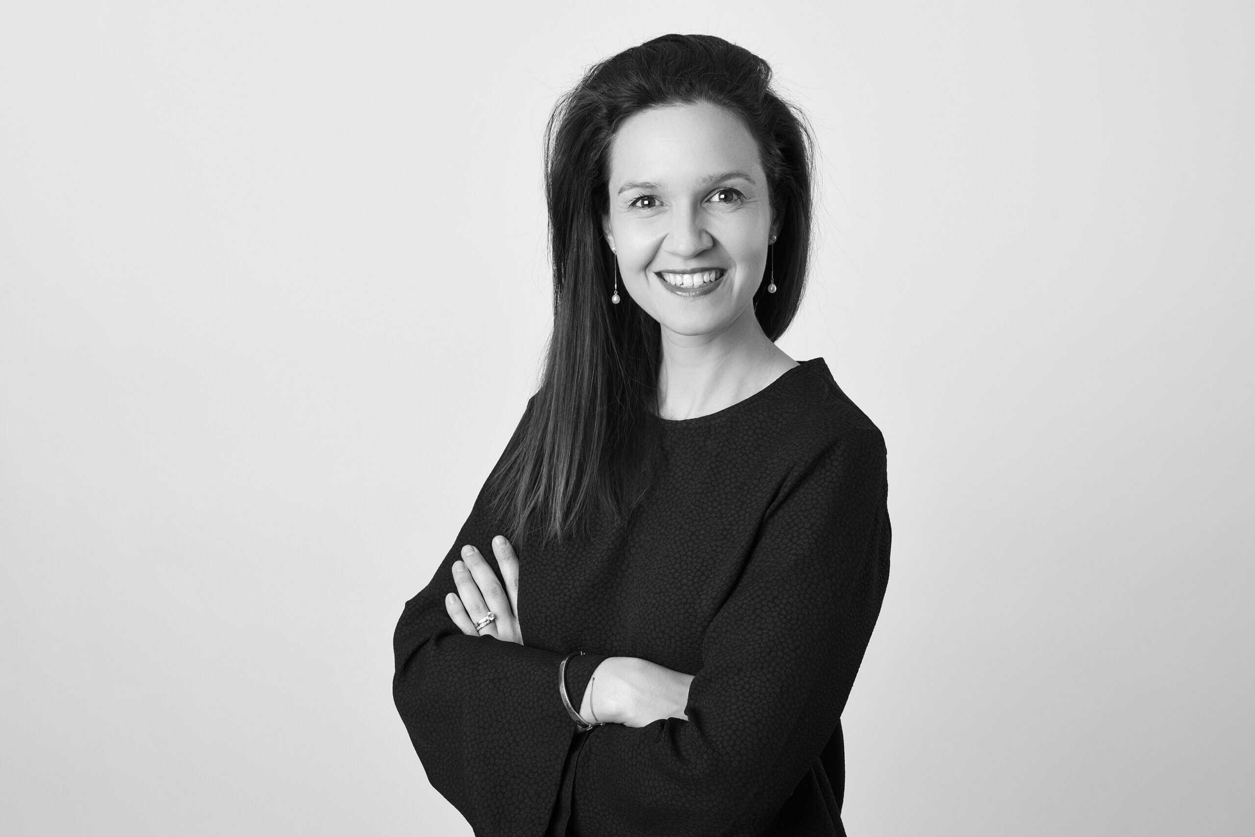 Femme d'affaires souriante en noir et blanc, portant une tenue professionnelle, avec un fond neutre, illustrant la confiance et le professionnalisme.