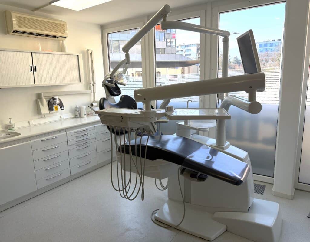 Salle de traitement dentaire équipée d'un fauteuil moderne, lampes et instruments pour soins dentaires professionnels dans un cabinet médical lumineux.